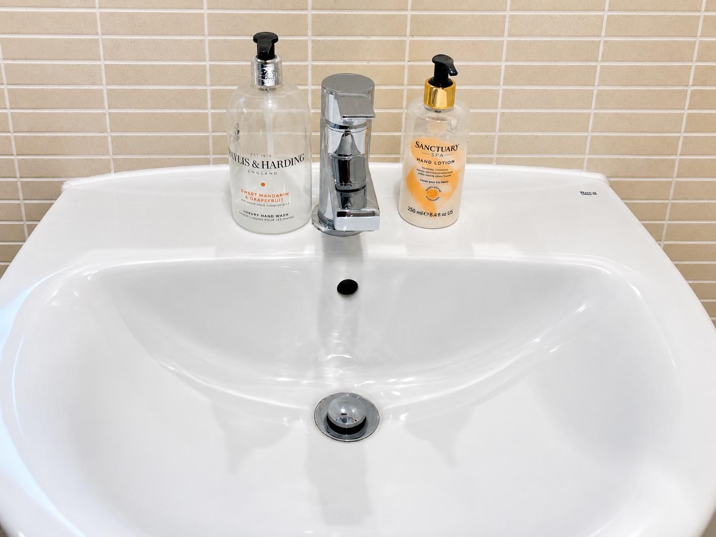 White basin and chrome mixer tap after cleaning, with original soap bottles retained